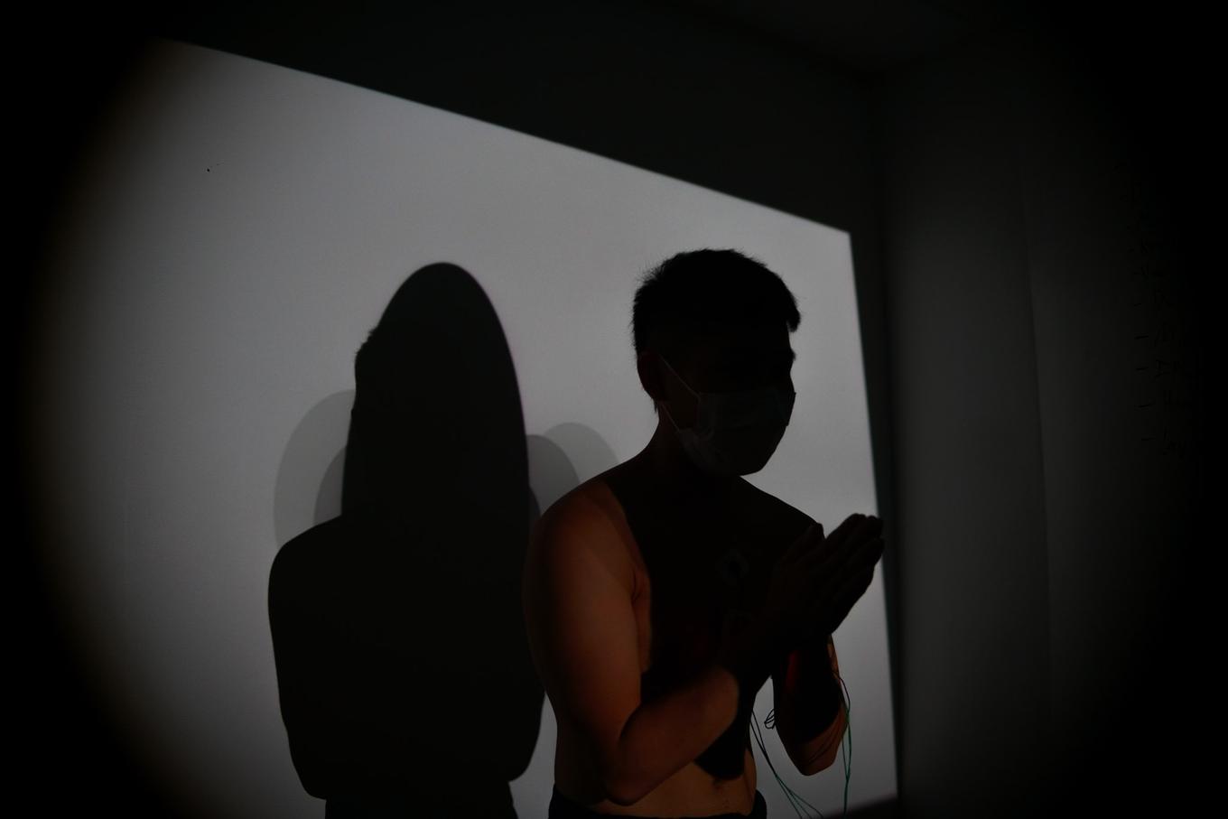 Silhouette of a dancer (Spencer), with hands clasped, facing 3/4 towards the camera. Spencer is in darkness, surrounded by a light background of projected light