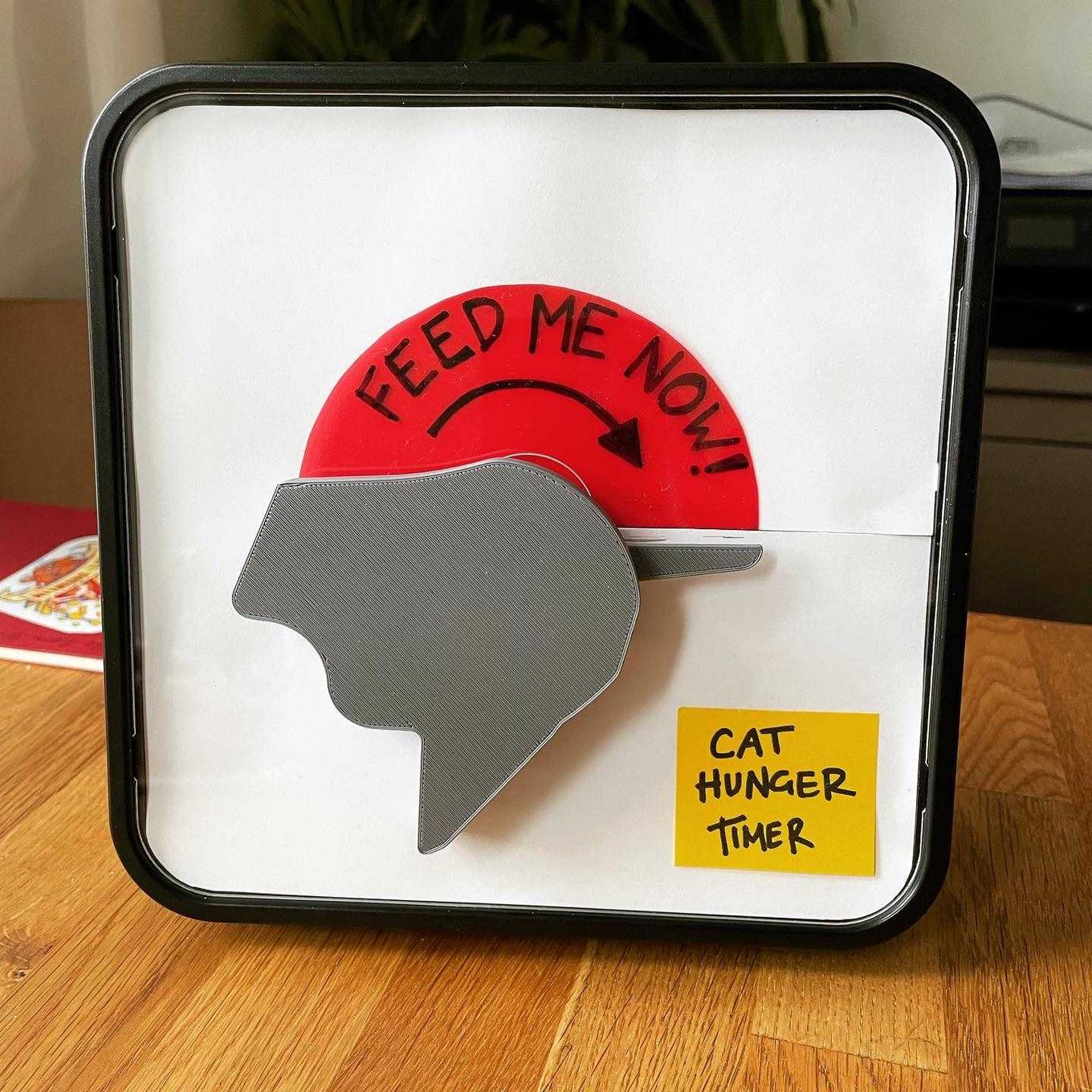 Image of a timer where the dial is a cat head. The mouth is open to 180 degrees, showing a red panel reading "FEED ME NOW!".