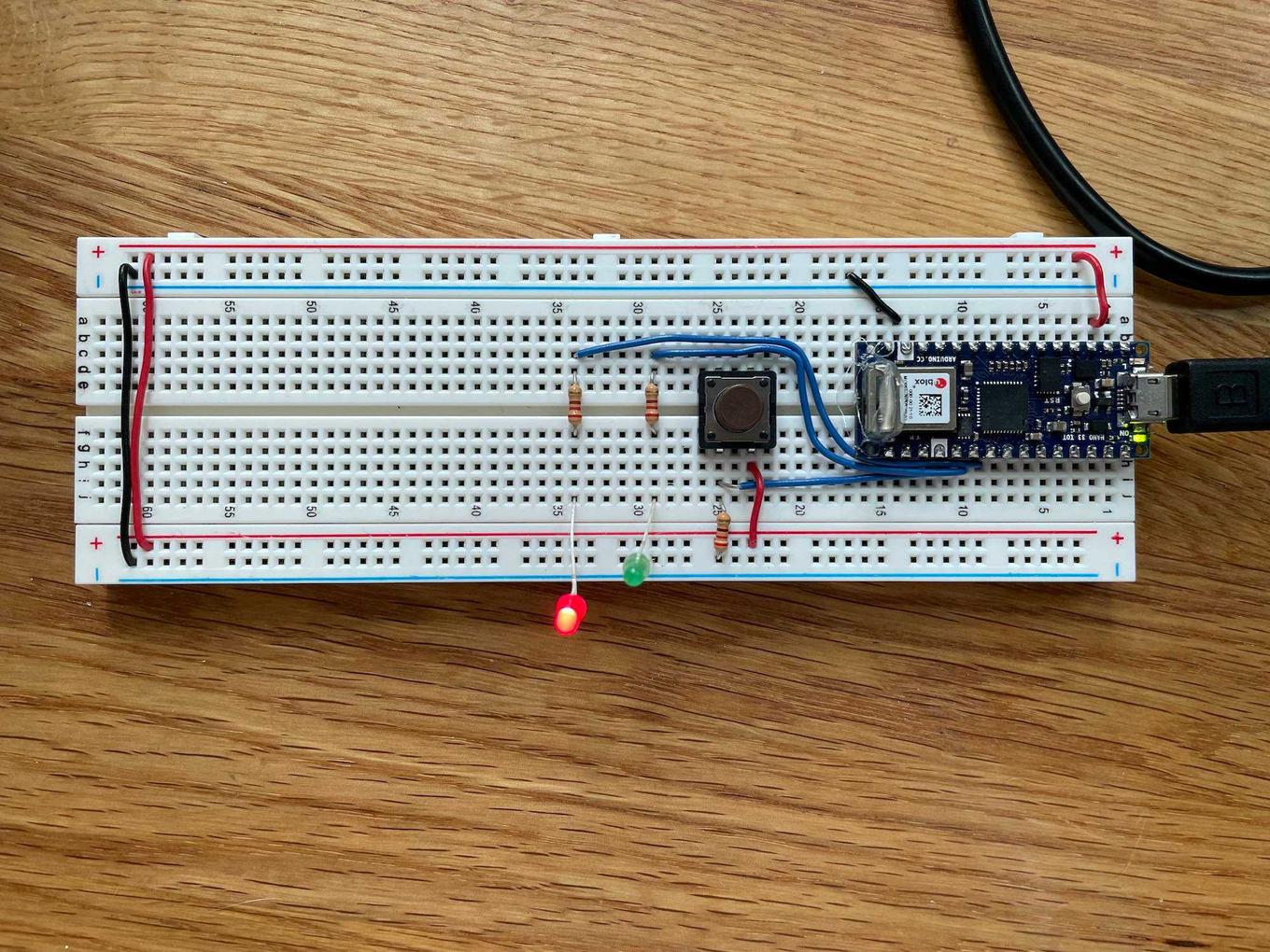 Breadboard with an Arduino Nano 33 IOT, button, and two LEDs (one red, one green). The red LED is lit.